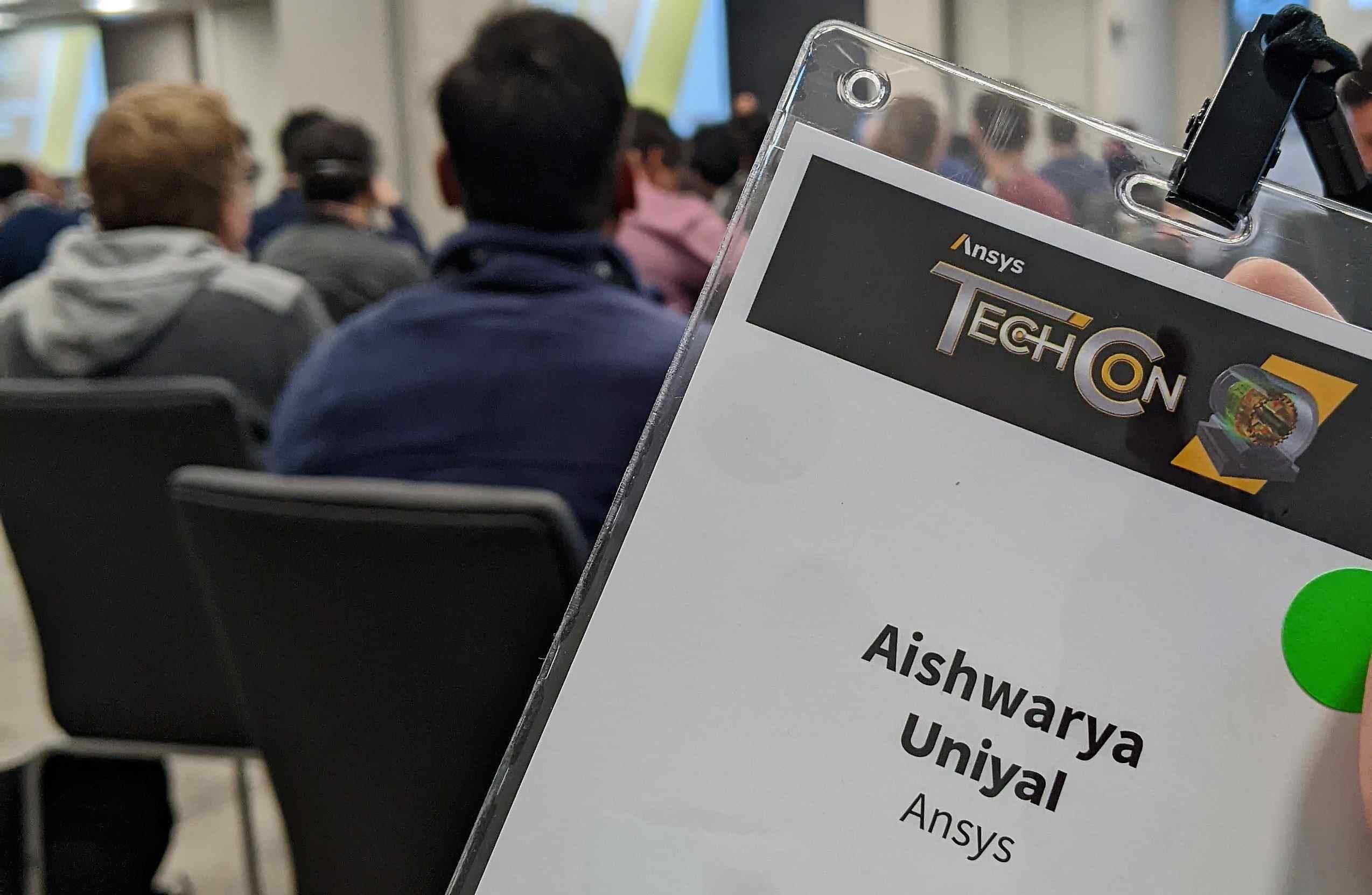 photograph of a conference pass held up against a crowd of attendees